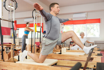 Man works out in gym on Pilates simulator. Sports club client performs exercise on reformer to...