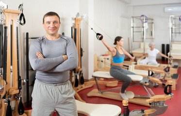 Smiling man after pleasant Pilates workout is standing in fitness room. Advertising poster for coaching services, gym, fitness activity