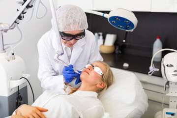 Focused skilled female cosmetologist performing hardware laser treatment to resurfacing and...