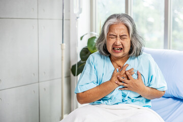 Asian senior old woman sitting on bed suffering from sudden heart attack and hold chest. Concept of...