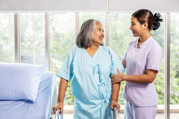 Female nurse helping elderly female with walking frame stand up from bed at home. Professional care for disabled patients, Disable old woman trying to walk with the assistance aid of female doctor