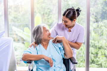 Portrait of young doctor or nurse and elderly patient pensioner on appointment at clinic or hospital, Asian woman in medical uniform and senior woman sitting on wheelchair and smile at each other