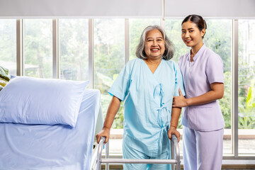 Female nurse helping elderly female with walking frame stand up from bed at home. Professional care for disabled patients,  Disable old woman trying to walk with the assistance aid of female doctor