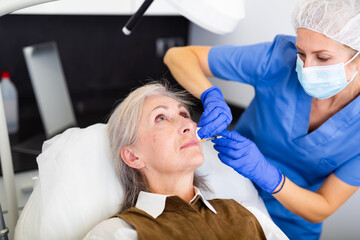 Closeup portrait of aged woman getting injections for face skin tightening at aesthetic cosmetology clinic ..