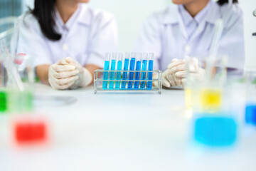 Fototapeta premium Half-body view of scientists talking with several research and experimental glass tubes containing a blue chemical solution. To produce biological medicine in the future for use in treating diseases.