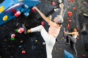 Determined old lady doing difficult wall climb in climbing gym