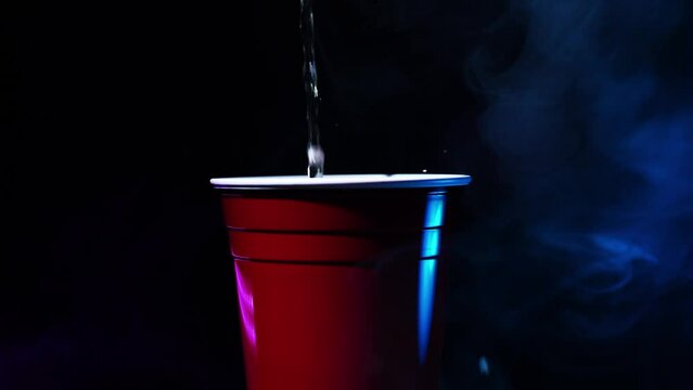 Pouring liquid into a red cup with party lights and smoke