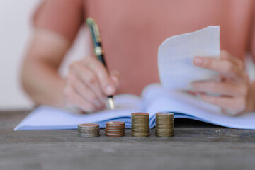 hand placing a coin into a white piggy bank on a table against a pale pink background.