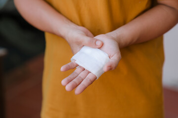 A person in a yellow top has white bandages on their hand and wrist because of a car accident.