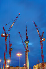 The famous Television Tower of Berlin at night with four red construction cranes
