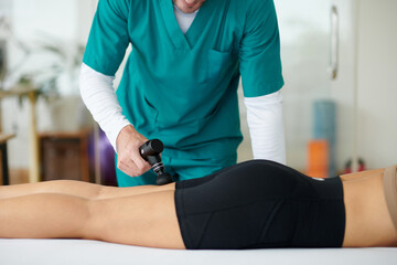 Therapist moving massage gun over bulk of hamstring muscles