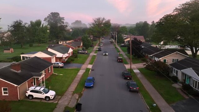 Car driving through quaint American neighborhood during foggy morning sunrise. Aerial view.