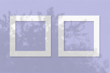 Natural light casts shadows from the leaves of a tree on 2 square frames of white textured paper lying on a lilac facture background. Mock up with an overlay of plant shadows