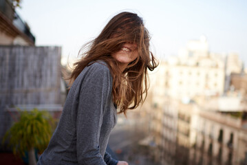 funny portrait of a young white and brunette woman with her hair covering her face during a windy day in Barcelona