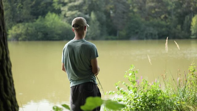 Young angler stands at the edge of murky lake surrounded by trees