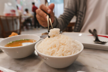 Person holding bowl of rice with a chopstick