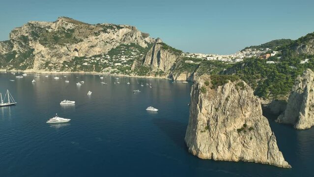 Drone panning shot of large sailing yachts anchored at Capri Rock on a sunny day.