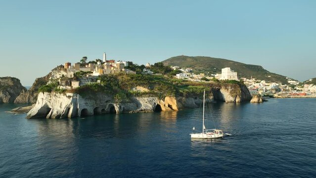 Drone panning shot of a sailing boat passing Grotta di Pilato on Isola di Ponza on a sunny day.