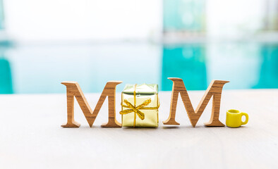 Mom wooden font with gift box and coffee cup on swimming pool edge, mother's day card background...