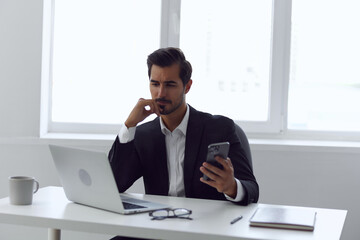 Man in office businessman sitting at desk and working in laptop and talking on phone, modern suit, finance and startup concept and data analysis, working lifestyle in bright office.