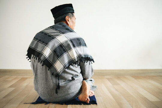 Asian Muslim man praying at mosque gesturing last movement of salat reciting salam to the right then to the left.