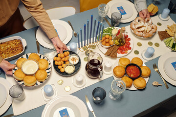 Above view of unrecognizable man and woman putting homemade snack on table served with tasty treats prepared for Hanukkah dinner