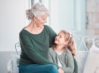 Obraz premium Grandmother, girl child and smile on sofa with hug, care or bonding for love, talk and family home lounge. Elderly lady, child and embrace with smile, relax and together on living room couch in house