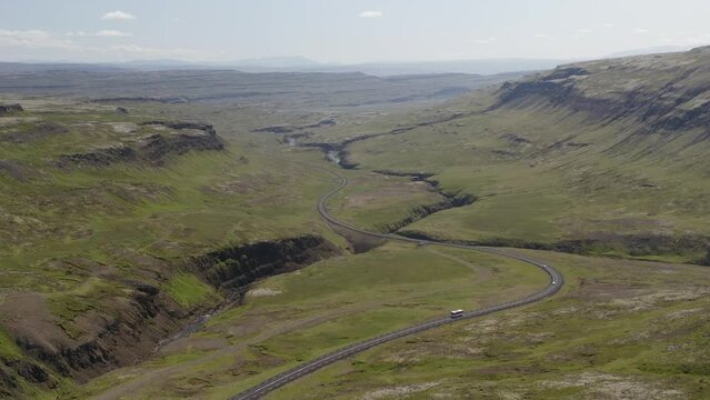 Aerial video as vehicles pass along a winding road cutting through lush green valley in Western Iceland
