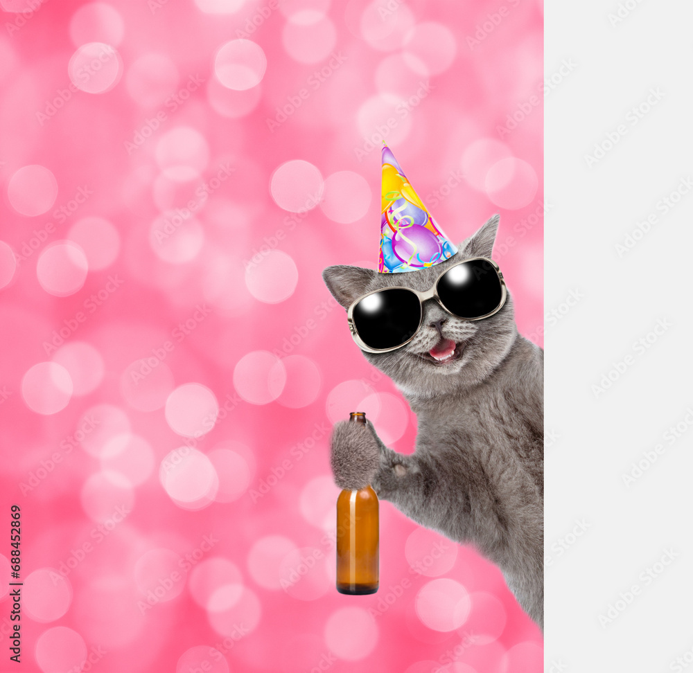 Poster Happy cat wearing birthday cap holds bottle of beer and look from behind empty board. Shade trendy color of the year 2023 - Viva Magenta background. Empty space for text