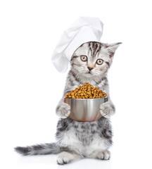 Funny tabby kitten wearing chef's hat holds bowl of dry food. isolated on white background