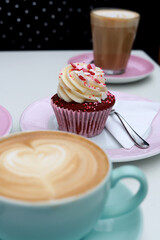Cupcake rouge avec de la crème et ses cafés sur de la vaisselle pastel en terrasse