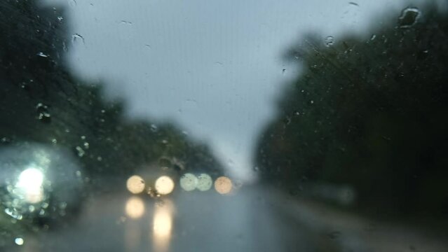 Glass rain auto. A car ride in a heavy downpour. Blurry traffic on the road, headlights of oncoming cars out of focus. The concept of bad weather, storm, hurricane. A gray, rainy, dreary autumn day.