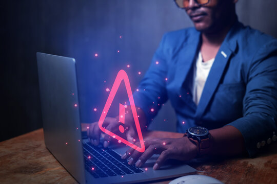 Businessman uses laptop computer with warning triangle sign or exclamation mark for error notification and technology maintenance concept.
