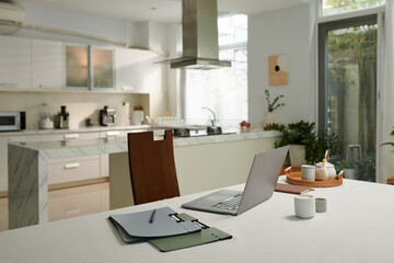 Opened laptop and folders on kitchen table, working from home concept