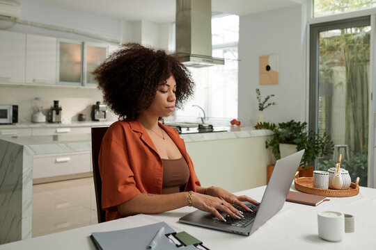 Serious Woman Working On Laptop At Kitchen Table At Home