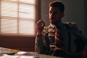 Young pensive man in retro formalwear thinking of something and smoking cigarette while sitting by...