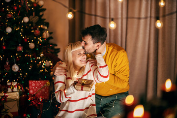 A loving couple is exchanging gifts and kissing while celebrating christmas and new year's eve at home.