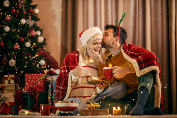 A happy couple is exchanging gifts and kissing on christmas eve and new year at home.