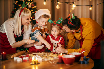 Children are making gingerbread cookies at home on christmas eve while parents helping them.