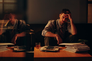 Tired young businessman in retro formalwear touching head and looking at stack of financial papers...