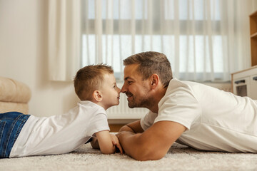 Father and his child are lying on the floor and rubbing noses and smiling at each other.