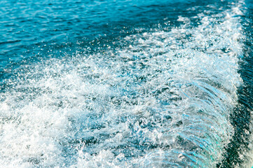 Waves on the sandy beach. Water background, blue sea water. Beautiful texture of sun glare on the water and sea foam.
