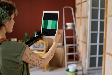 Rear view of young woman with prosthetic arm choosing color online on tablet pc for design of new house