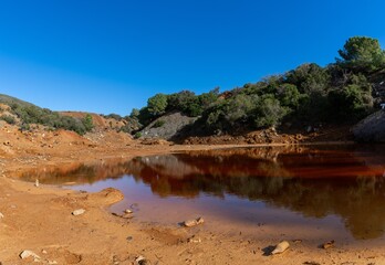 landscape view of a red waste water pond in an abandoned iron ore mine on Elba