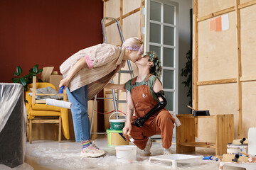 Lesbian couple kissing while painting wall in their new apartment