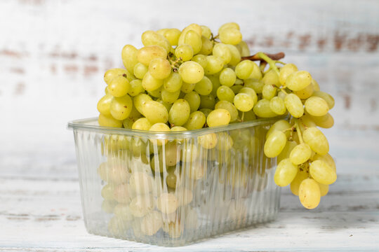 Packed green grapes on a white wooden background. Organic agricultural products. Delicious bunch of grapes