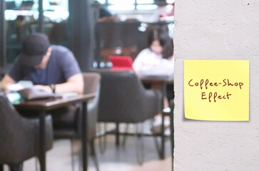 People in cafe with stick note on wall written Coffee-Shop Effect - working in coffee shops seems...