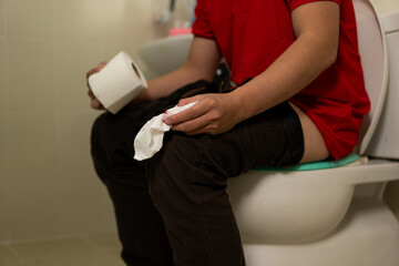 Man holding toilet tissue roll in bathroom Young man has diarrhea holding his bum on bathroom...