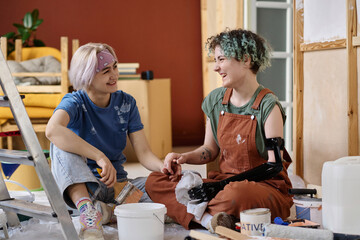 Happy friends sitting on the floor and talking to each other while resting after repair