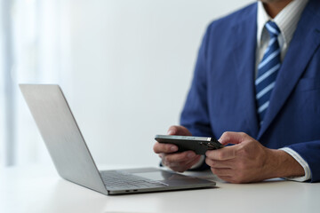 Businessman holds smartphone, checks email, checks job details on Laptop computer on white desk to point to successful business goals in office.